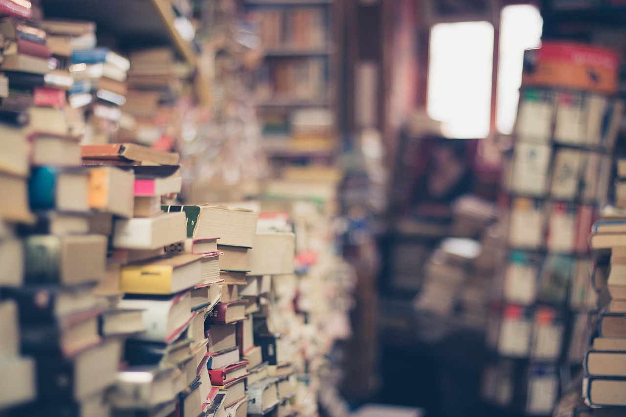 Des piles de livres entassées dans une librairie, avec des rayonnages flous à l’arrière