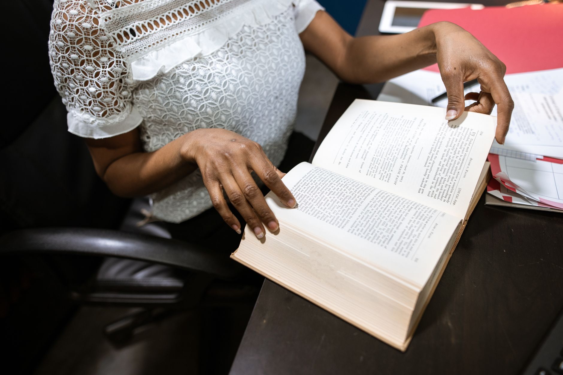 Une personne assise à un bureau feuillette un livre volumineux ouvert.
